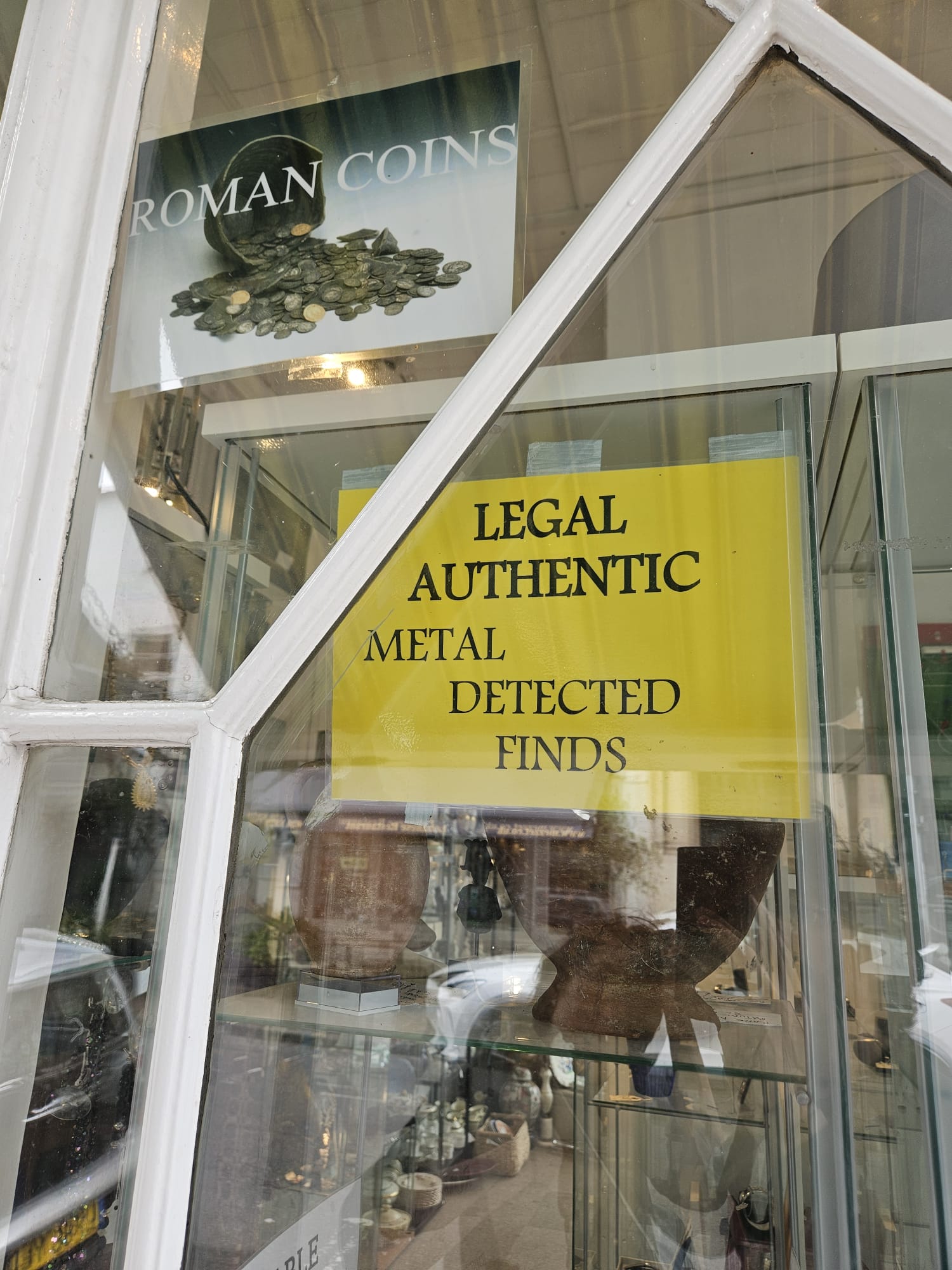 Yellow and purple image of a sign in an antiquities dealer shop stating legal authentic metal detected finds for sale, as well as Roman coins