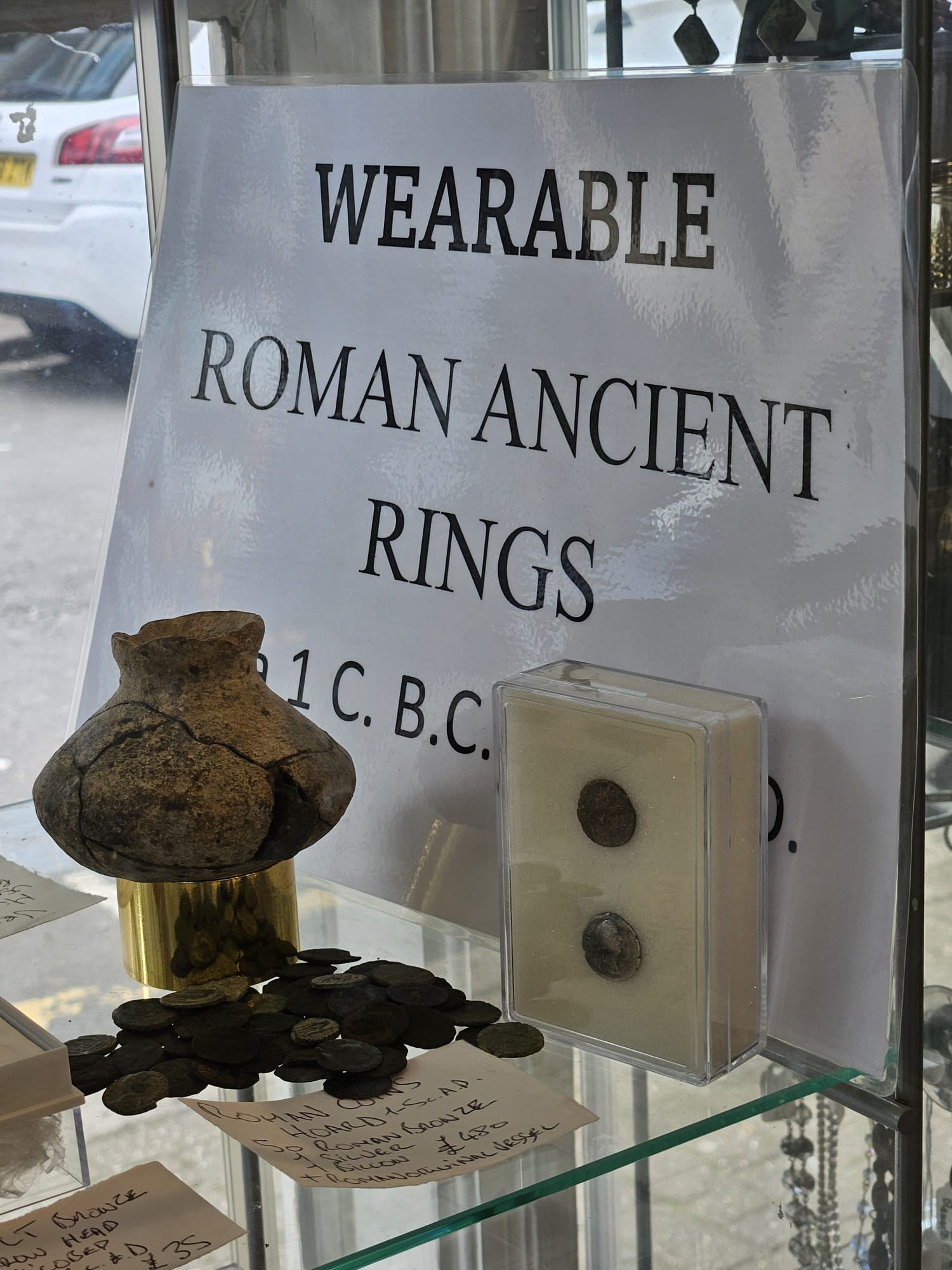 Purple and yellow filtered image of a sign saying 'wearable Roman Ancient Rings' alongside ancient Roman coins and pottery for sale.